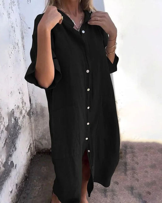 A woman wearing a black button-down dress with 3/4 sleeves and side - pockets.  Comes in Grey